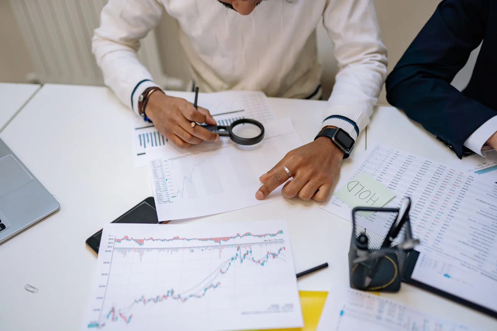 Business professionals reviewing charts with a magnifying glass in an office setting. Which secondary market research questions matter most