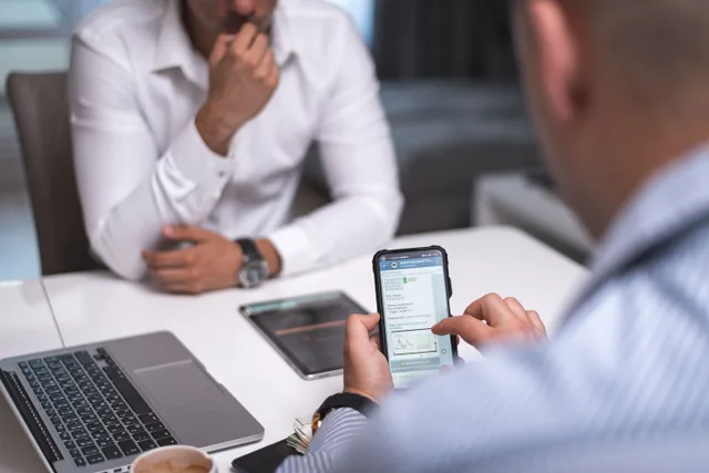 Two businessmen in a meeting room using a smartphone and laptop for a professional discussion. DIY vs. Agency Consumer Research: A Cost Comparison for US Teams