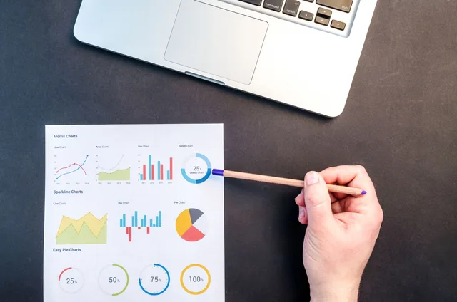 Hand holding pencil reviewing colorful data charts on desk with laptop. 9 points on choosing market research surveys tools